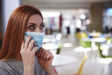 Photo of Woman with medical mask talking on mobile phone in cafe. Virus protection