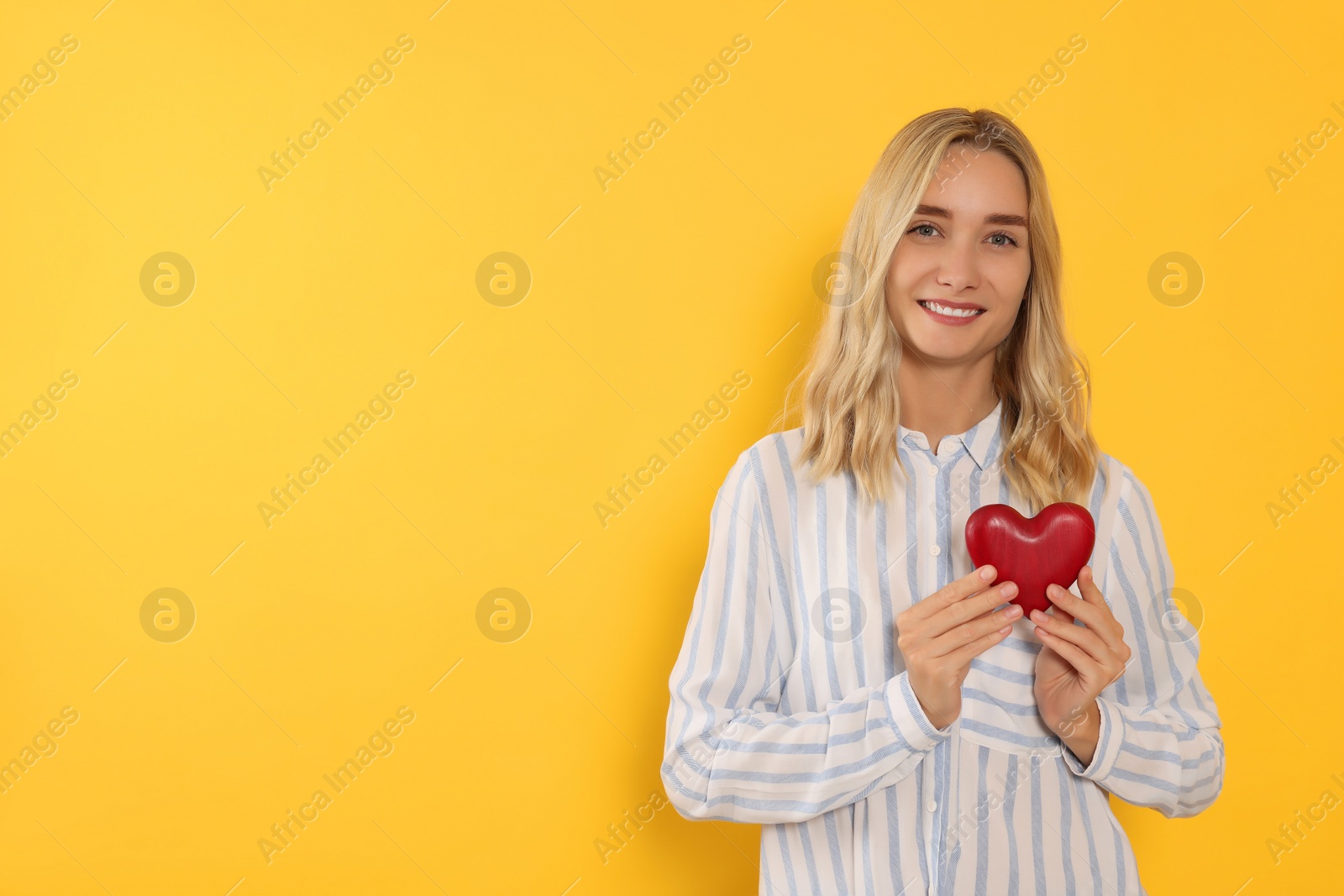 Photo of Happy volunteer holding red heart with hands on orange background. Space for text