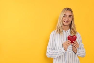 Happy volunteer holding red heart with hands on orange background. Space for text