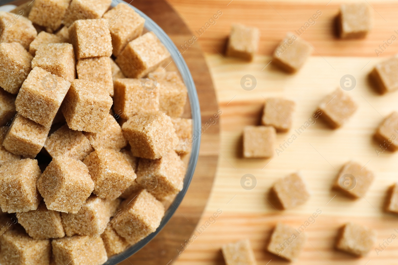 Photo of Brown sugar cubes in bowl on wooden table, top view