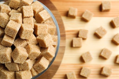 Photo of Brown sugar cubes in bowl on wooden table, top view