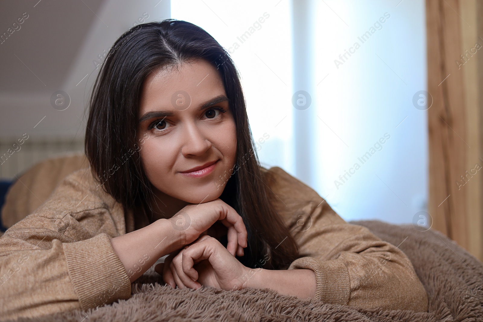 Photo of Portrait of beautiful young woman lying on bed at home, space for text