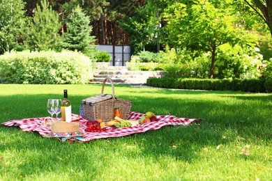 Picnic basket with products and bottle of wine on checkered blanket in garden. Space for text