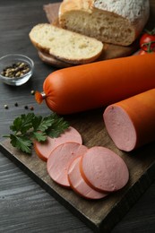 Photo of Board with tasty boiled sausages on dark wooden table