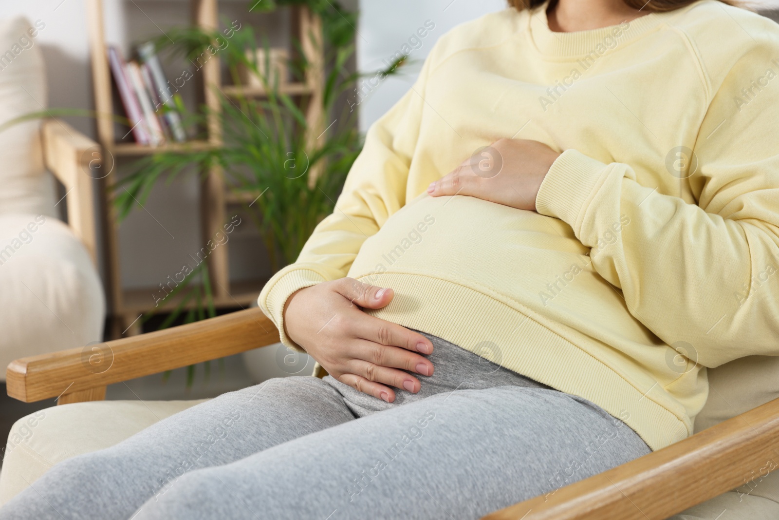 Photo of Pregnant woman touching belly in living room, closeup