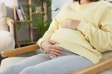 Pregnant woman touching belly in living room, closeup