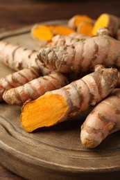 Photo of Many fresh turmeric roots on wooden board, closeup