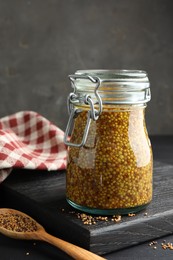 Photo of Whole grain mustard in jar and dry seeds on black table