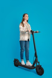 Photo of Happy woman riding modern electric kick scooter on light blue background