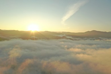 Photo of Aerial view of beautiful mountains covered with fluffy clouds at sunrise