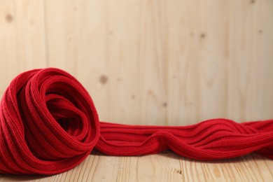 Red knitted scarf on wooden table, space for text