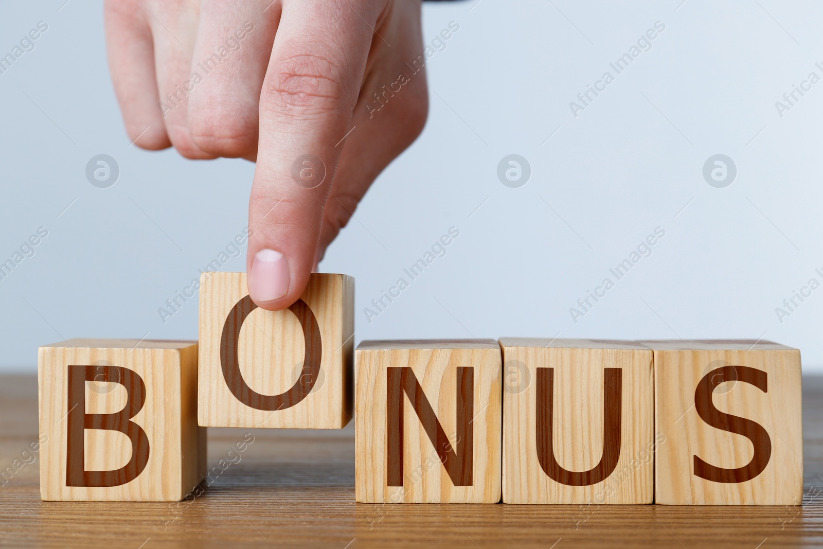 Image of Man making word Bonus of cubes with letters on wooden table, closeup