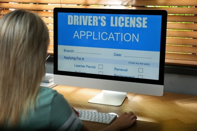 Photo of Woman using computer to fill driver's license application form at table in office, closeup