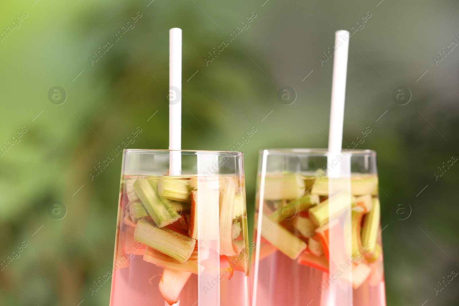 Photo of Glasses of tasty rhubarb cocktail outdoors, closeup