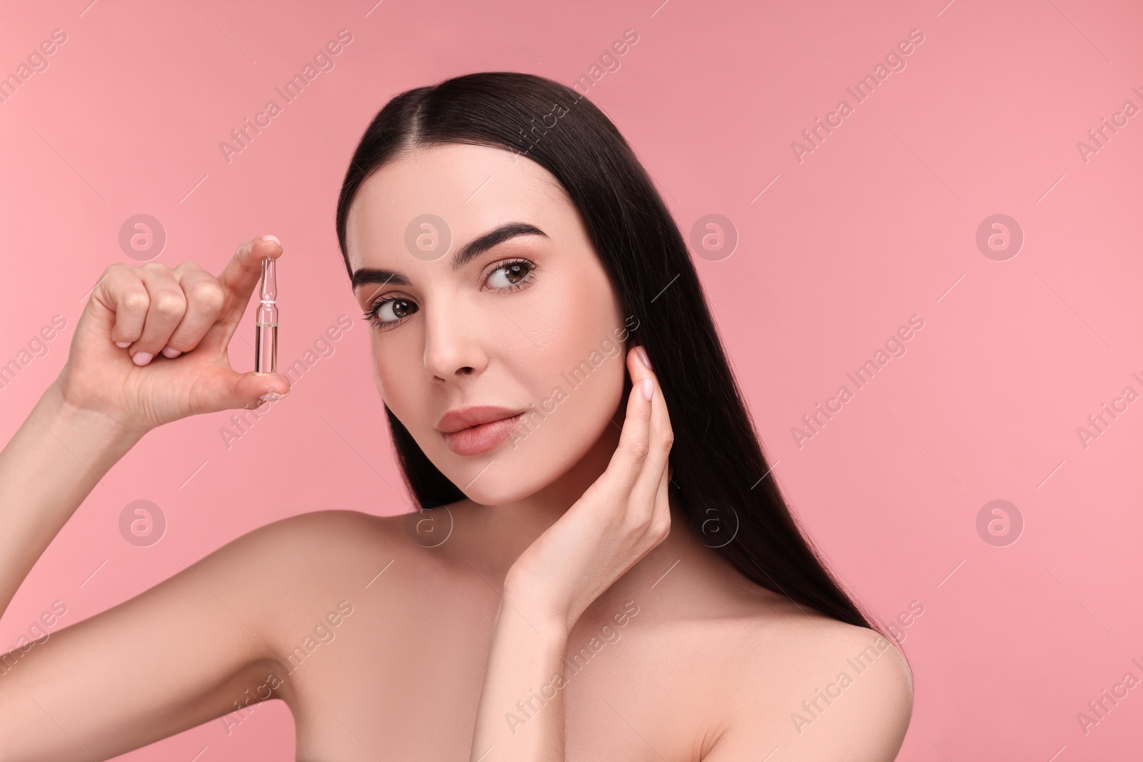 Photo of Beautiful young woman holding skincare ampoule on pink background