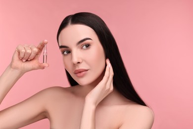 Beautiful young woman holding skincare ampoule on pink background