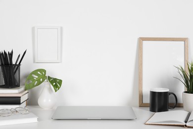 Cozy workspace with laptop, houseplants and stationery on white desk at home