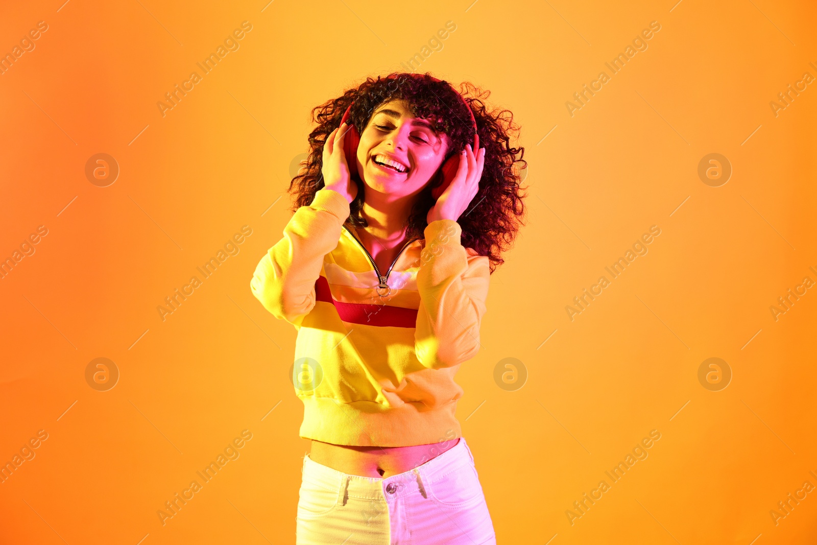 Photo of Beautiful young woman listening to music with headphones on color background in neon lights