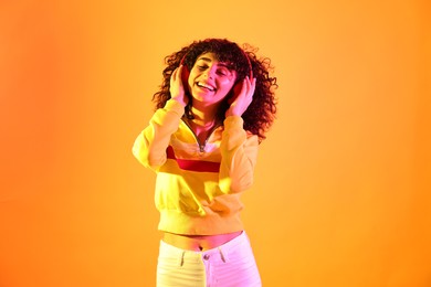 Beautiful young woman listening to music with headphones on color background in neon lights