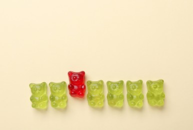 Photo of Red jelly bear among green ones on beige background, flat lay. Uniqueness concept