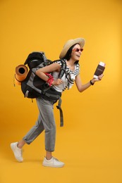 Happy female tourist with passport, ticket and backpack on yellow background