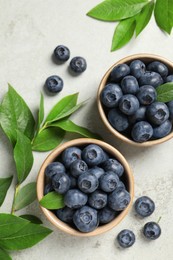 Tasty fresh blueberries with leaves in bowls on light grey table, flat lay