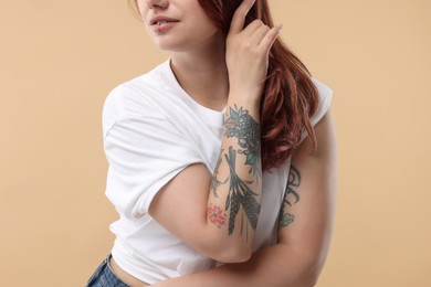 Woman with cool tattoos on beige background, closeup