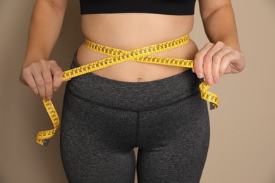 Photo of Woman measuring waist with tape on beige background, closeup