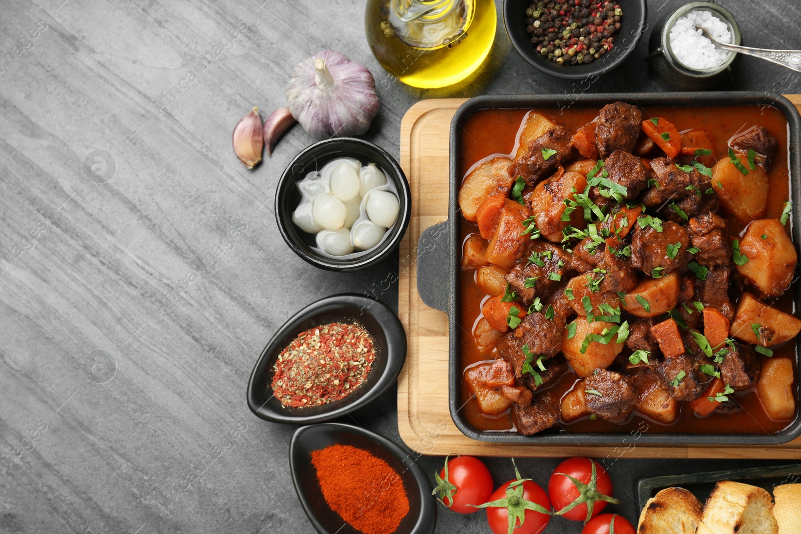 Photo of Delicious beef stew and ingredients on grey table, flat lay. Space for text