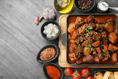 Delicious beef stew and ingredients on grey table, flat lay. Space for text