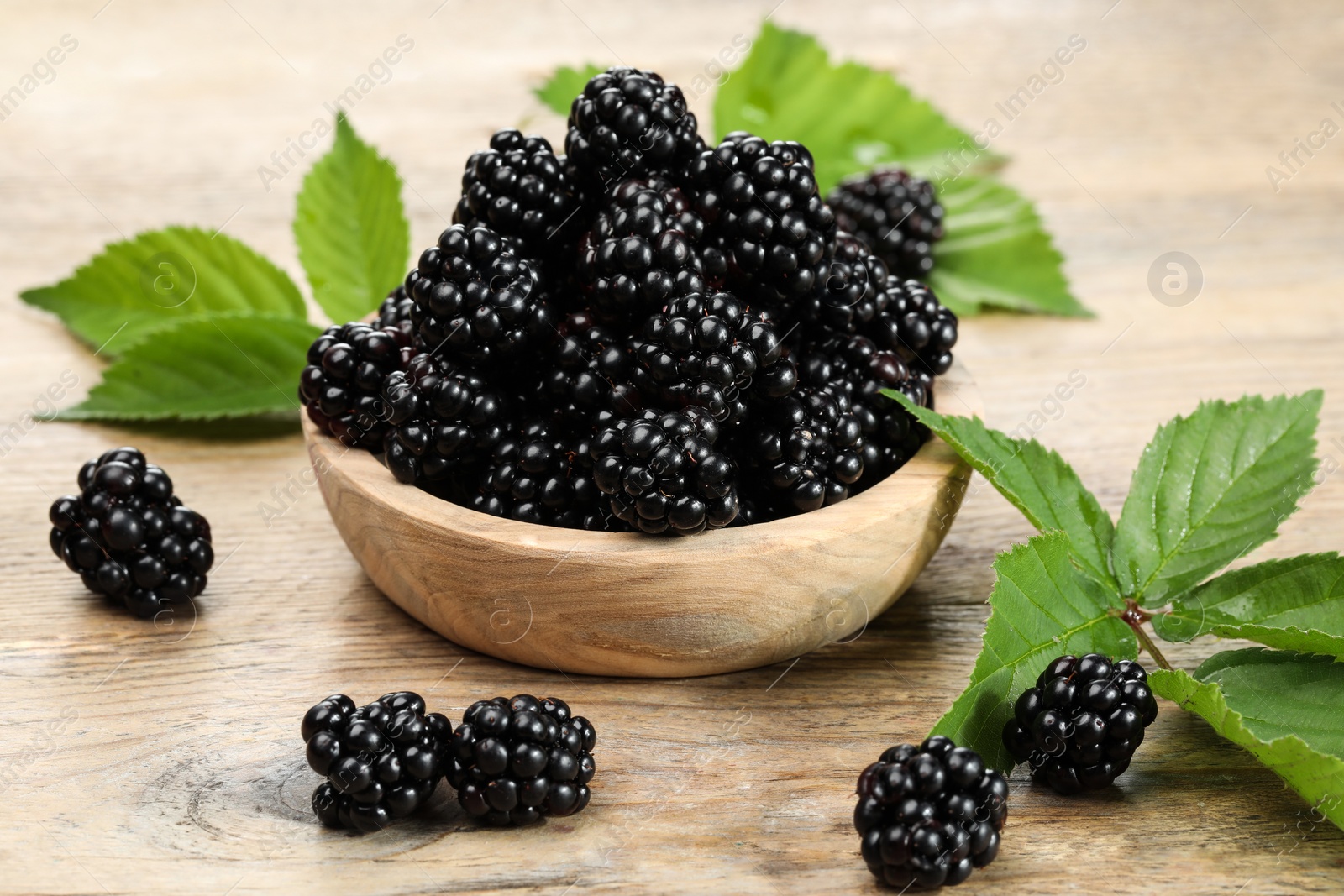 Photo of Ripe blackberries and green leaves on wooden table, closeup