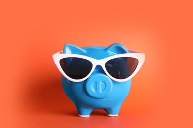 Piggy bank with sunglasses on color background. Travel agency