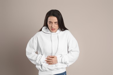 Photo of Young woman suffering from stomach ache on beige background. Food poisoning