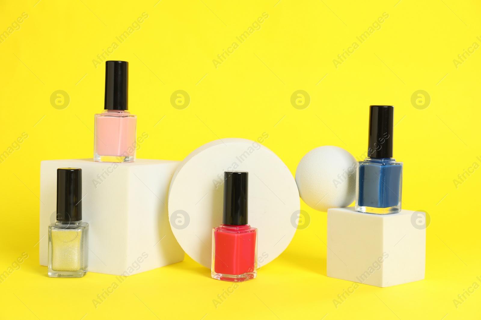 Photo of Stylish presentation of bright nail polishes in bottles on yellow background