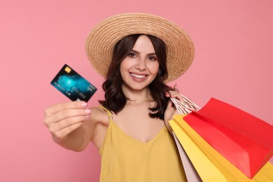 Beautiful young woman with paper shopping bags and credit card on pink background