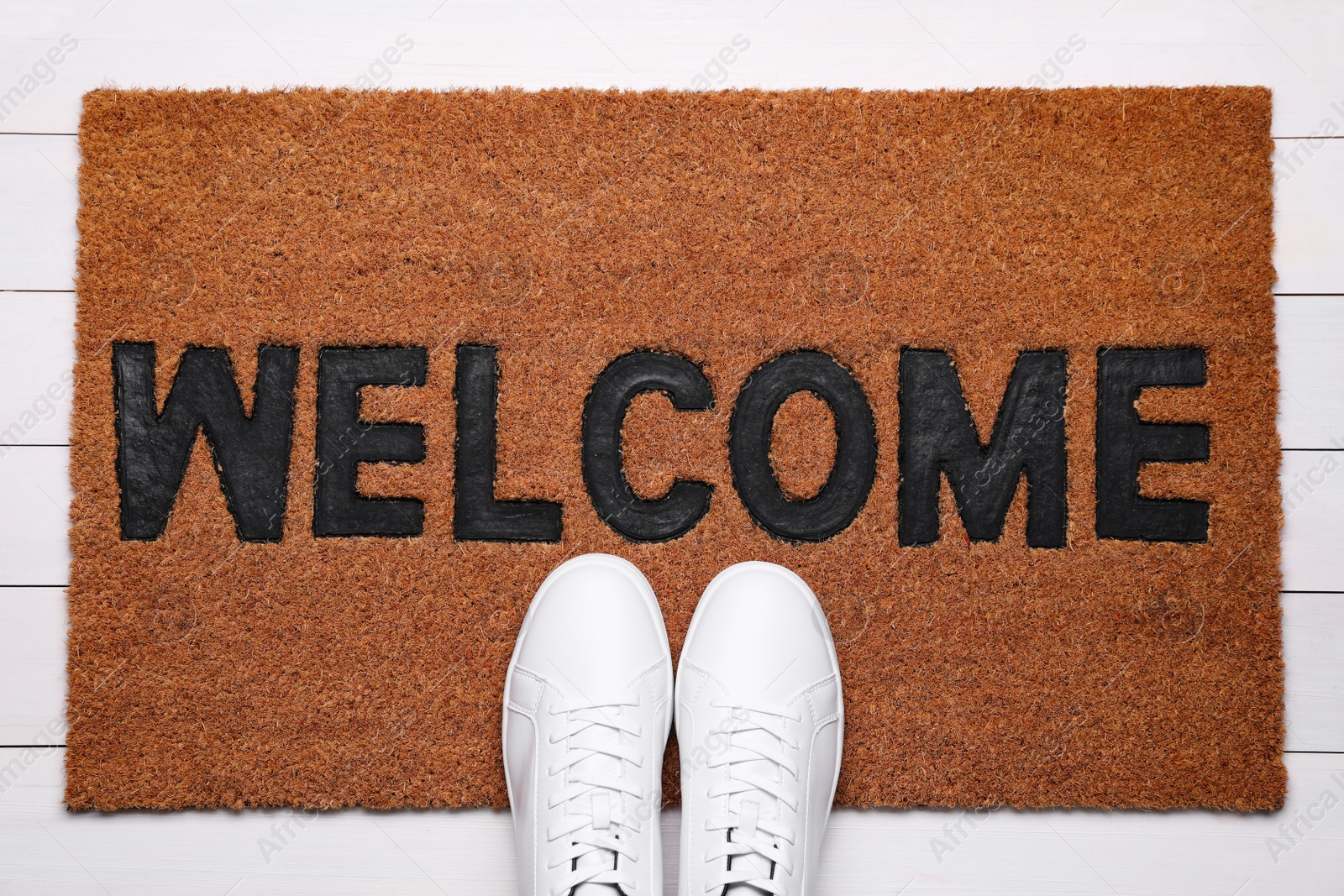 Photo of New clean mat with word WELCOME and shoes on floor, top view