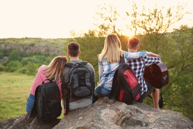 Photo of Group of young people with backpacks and guitar in wilderness. Camping season