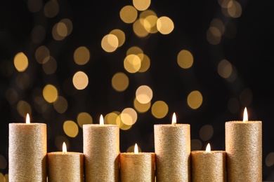 Photo of Golden candles burning against defocused lights, closeup. Space for text