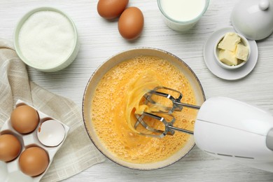 Photo of Beating eggs in bowl with mixer at white wooden table, flat lay