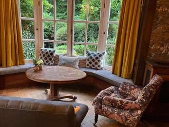 Photo of Wooden table near bay window seat with cushions in cozy room. Interior design