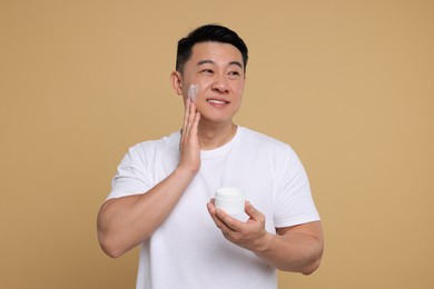 Photo of Handsome man applying cream onto his face on light brown background