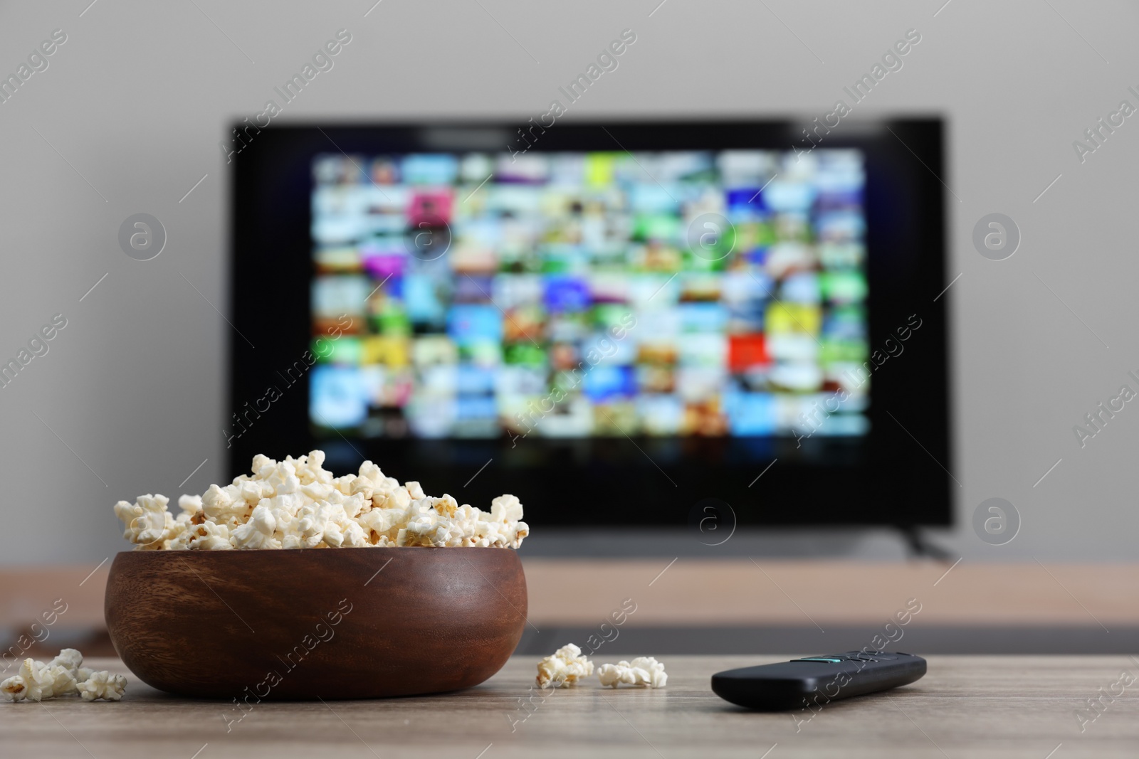 Photo of Bowl of popcorn and TV remote control on table indoors. Space for text