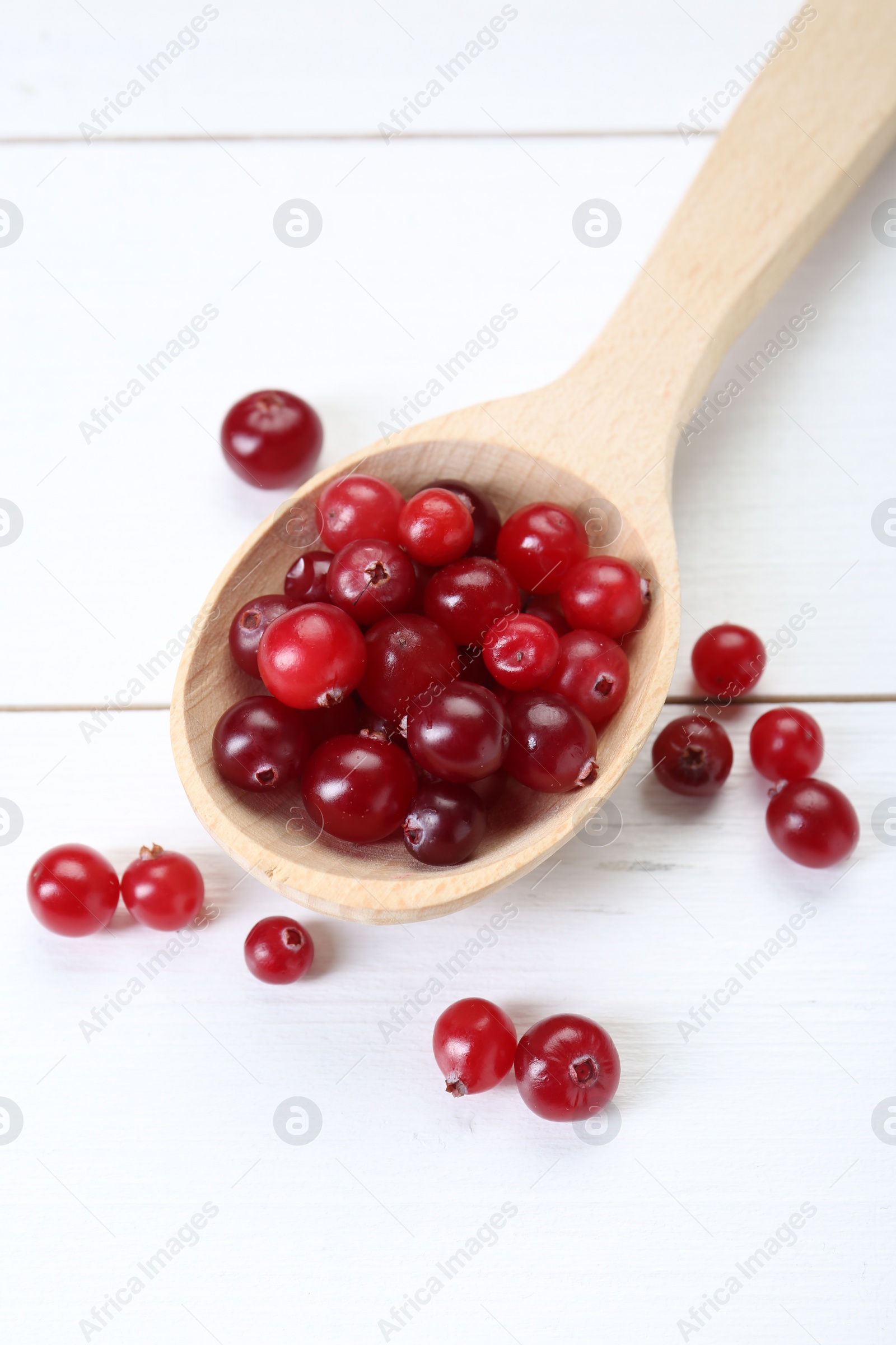 Photo of Spoon with fresh ripe cranberries on white wooden table, top view