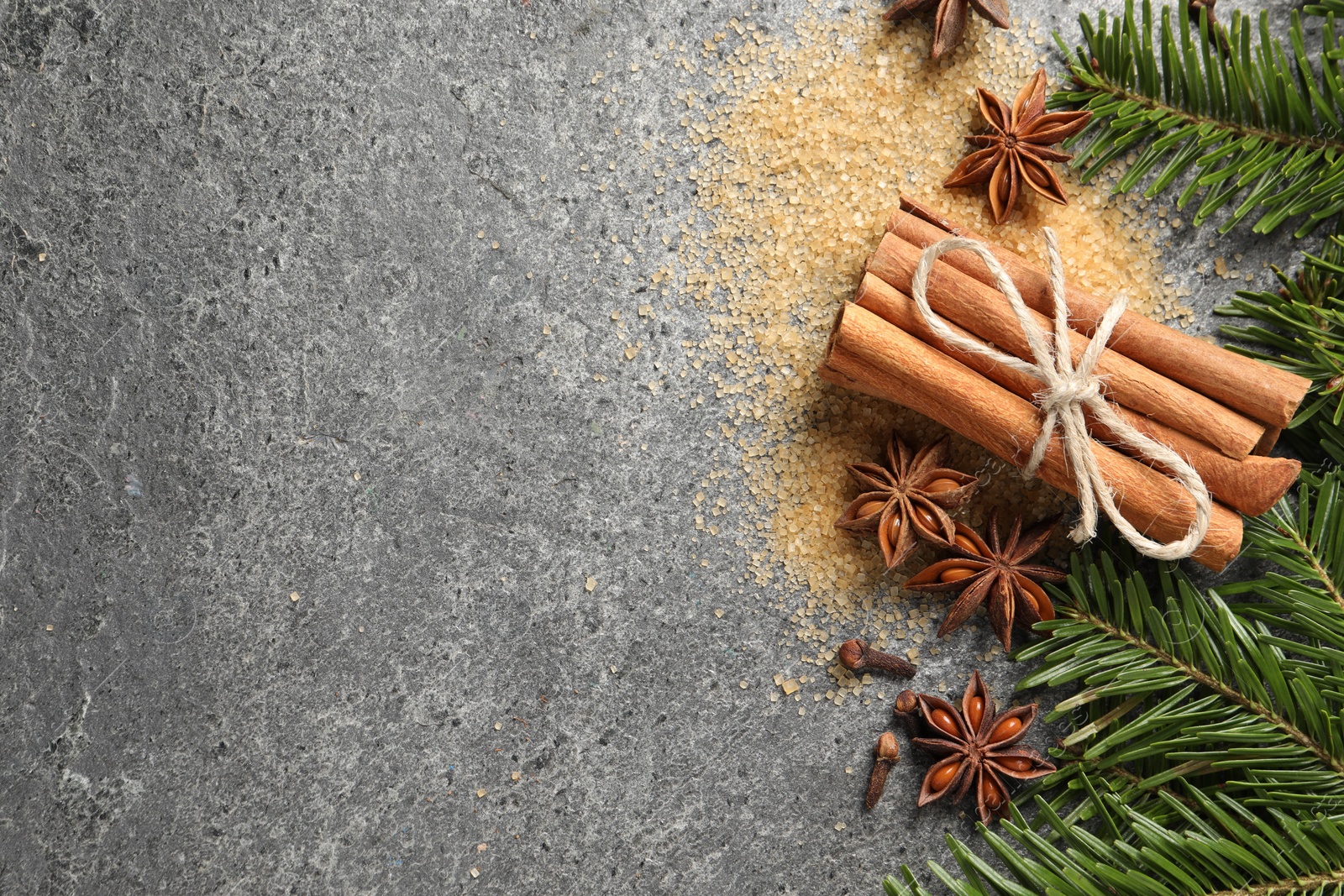 Photo of Different spices and fir branches on gray table, flat lay. Space for text