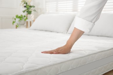 Woman touching soft white mattress on bed indoors, closeup