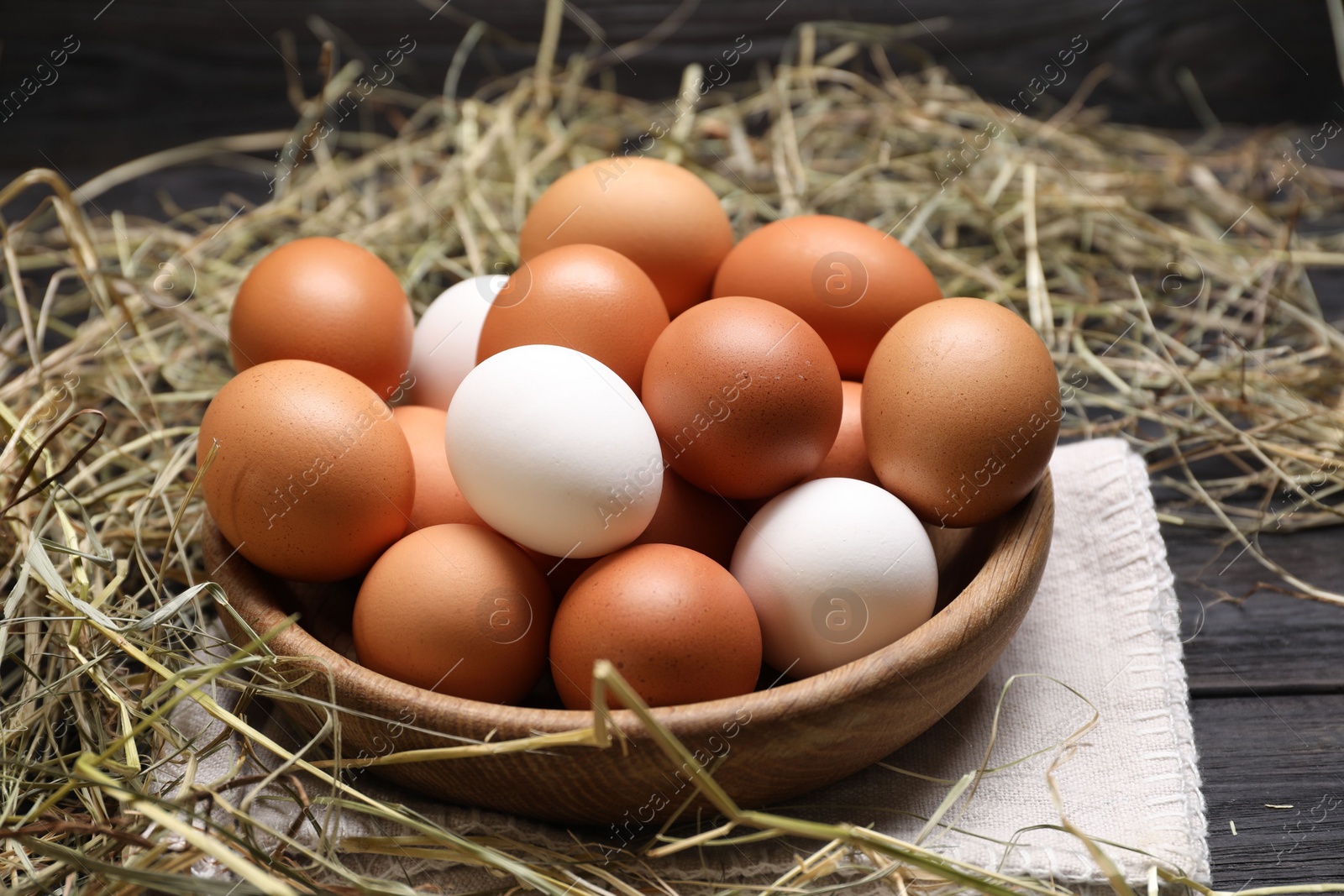 Photo of Fresh chicken eggs in bowl and dried hay on black wooden table