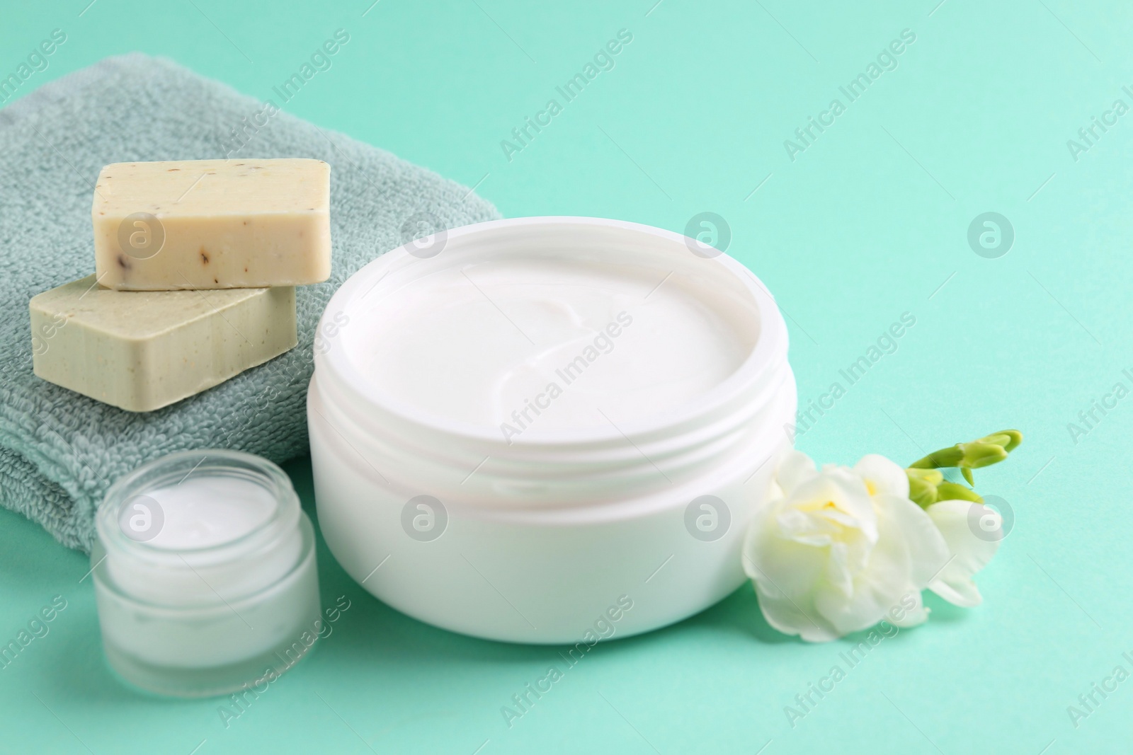 Photo of Moisturizing cream in open jars, soap bars and freesia flower on turquoise background. Body care products