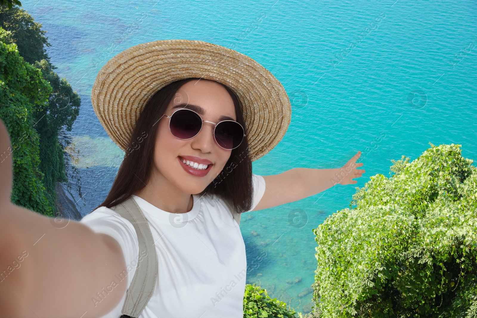Image of Smiling young woman in sunglasses and straw hat taking selfie on green hill near sea