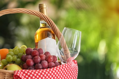 Picnic basket with products and wine on blurred background, space for text