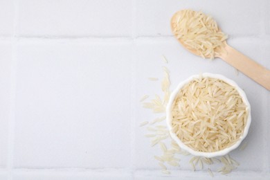 Bowl and spoon with raw rice on white tiled table, flat lay. Space for text